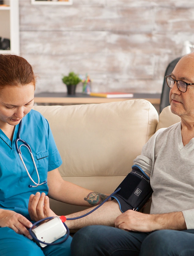 Home healthcare nurse taking an elderly male patient's blood pressure using a manual monitor in his living room.